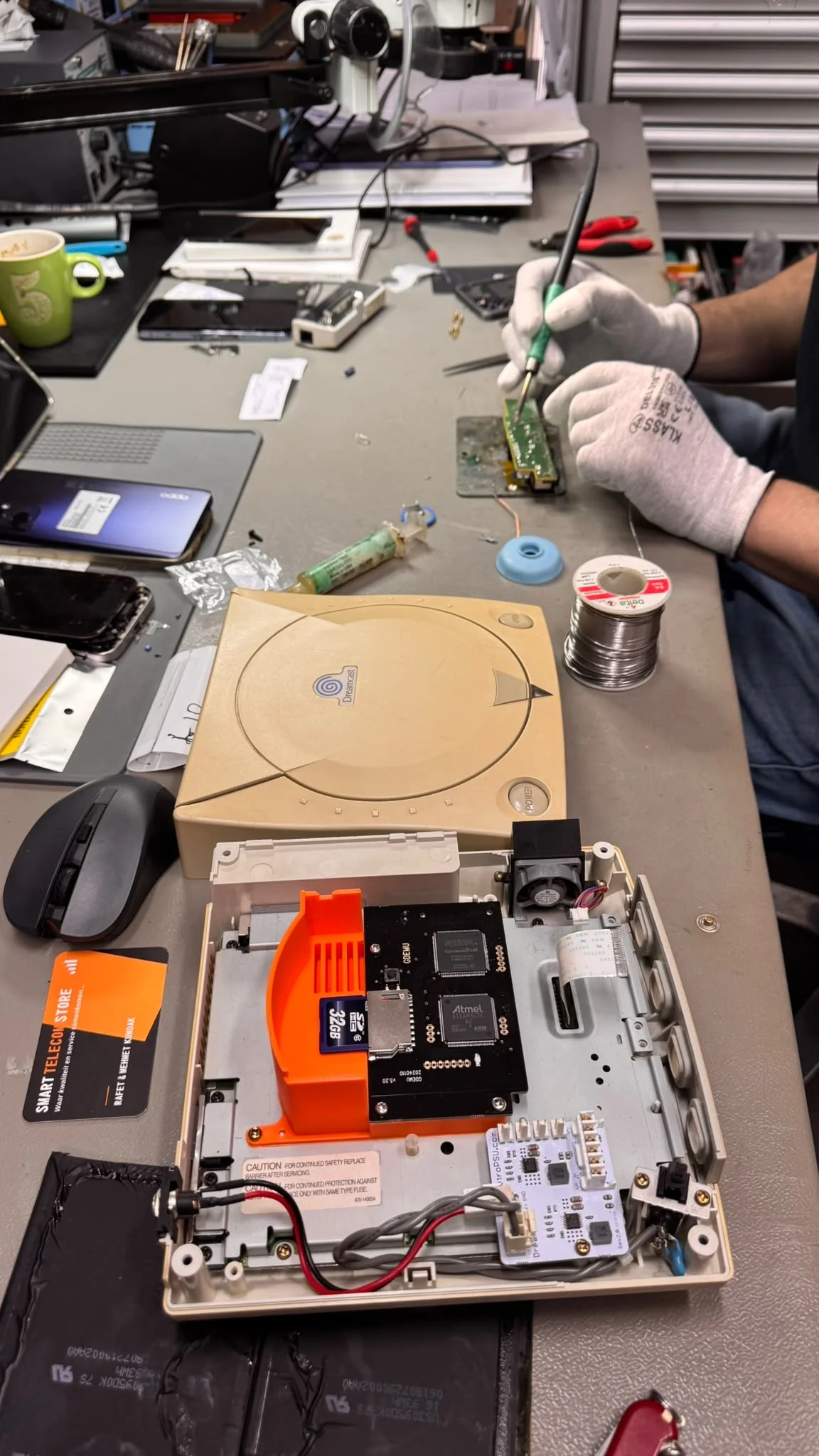 Geopende Sega Dreamcast en soldeerwerk aan een printplaat bij Smart Telecom Store in Alphen aan den Rijn
